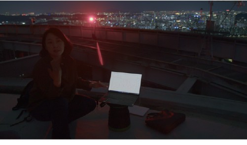 A researcher works with monitoring equipment on a city rooftop at night.